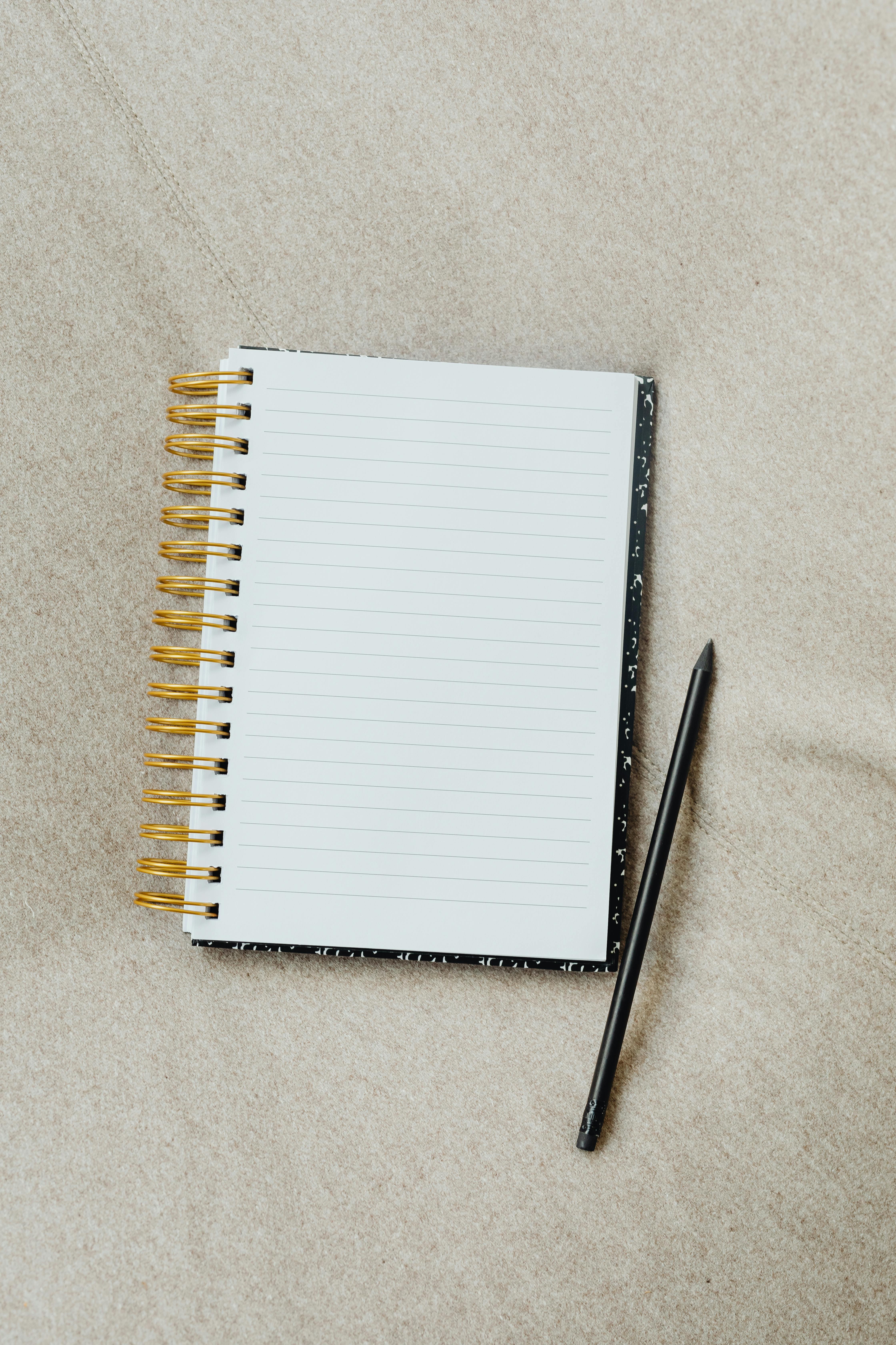 Flatlay of a blank spiral notebook and pencil on a beige textured surface.